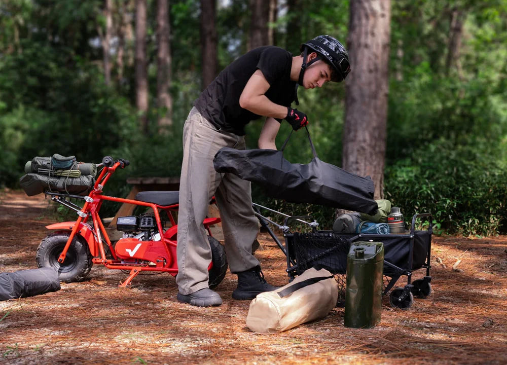 Person setting up camping gear in a forest with a red gmb100 u mini bike.