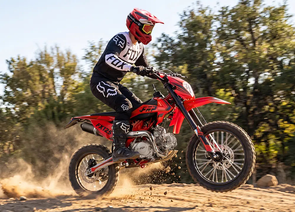 Person riding a red dirt bike on a dirt track with trees in the background