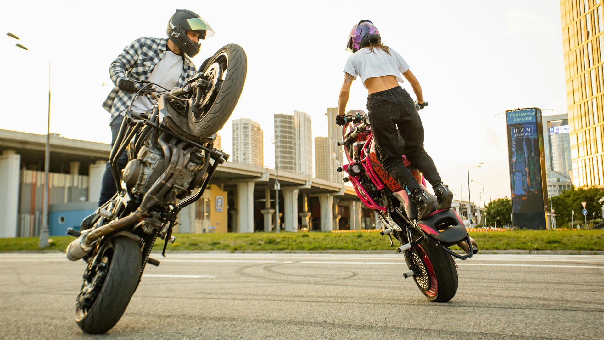 A man and a women are doing wheelies on their motorbikes.