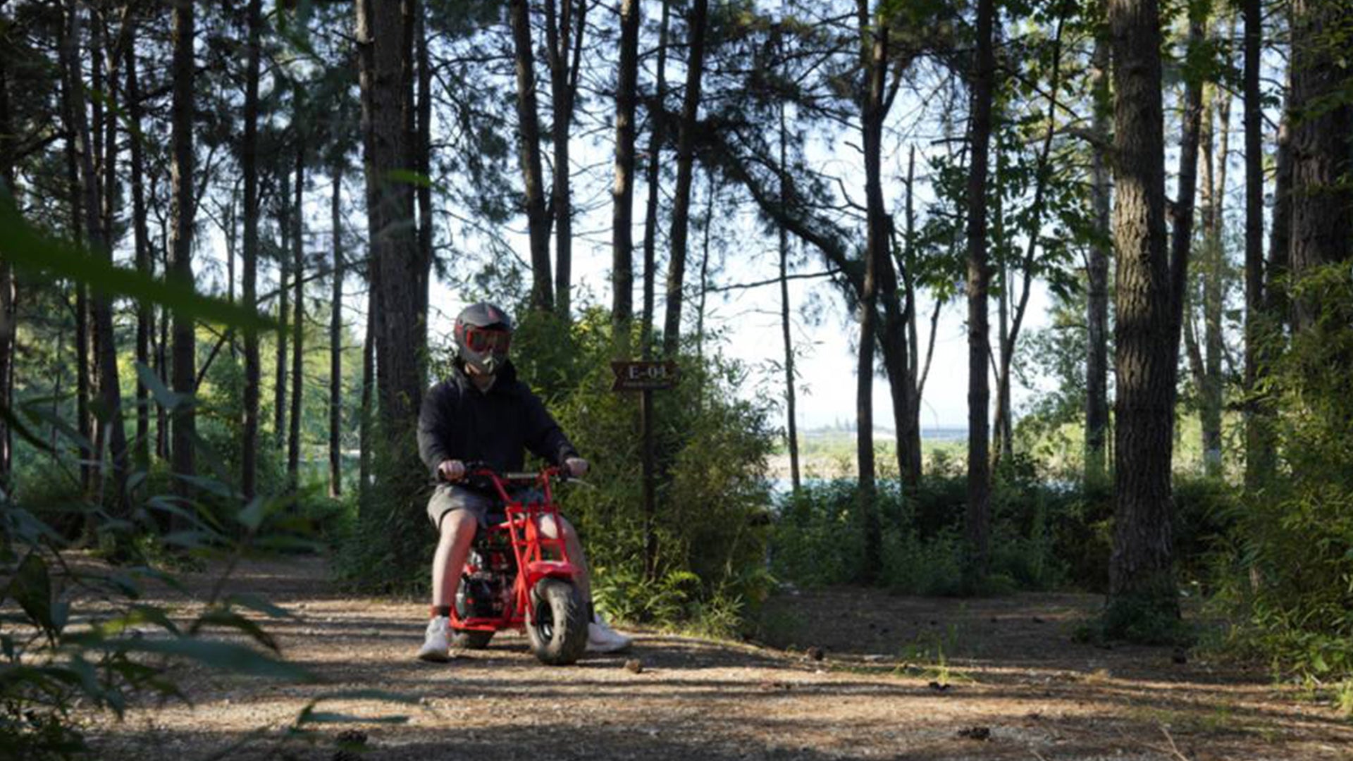 A man is riding a GMB100 gas mini bike in the forest.