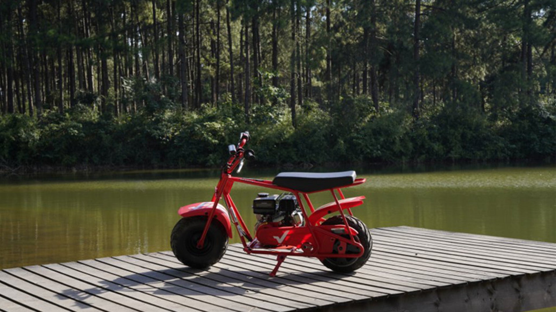 A GMB100 gas mini bike is in the forest near the lake.