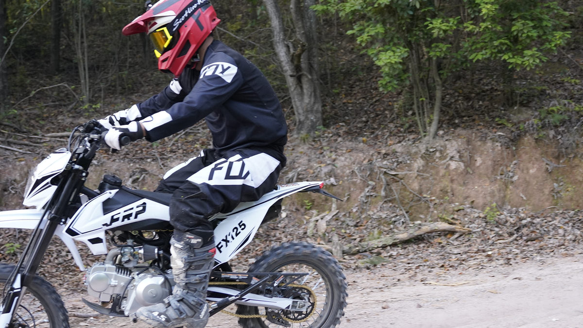 Rider in full motocross gear on a white FRP FX125 125cc dirt bike on a forest dirt trail