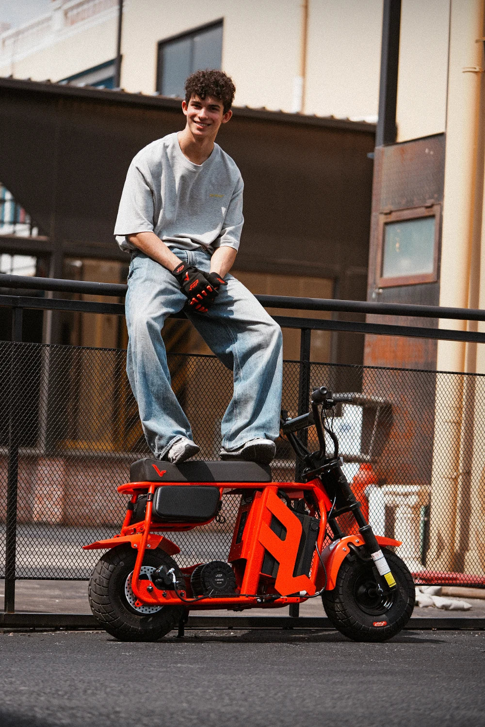 Teen sitting on a railing with his feet on an orange FRP M3 electric mini bike